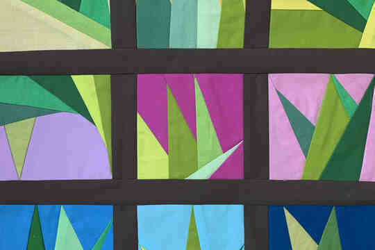 A quilting pattern with several green triangles in different square panels