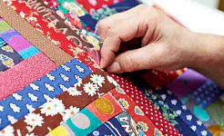 A person sews a quilt from many different pieces of fabric